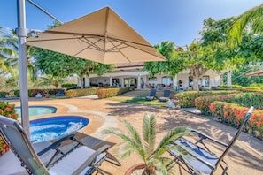 Un espace piscine comprenant des chaises longues, un jacuzzi et un coin salon couvert avec vue sur la piscine.