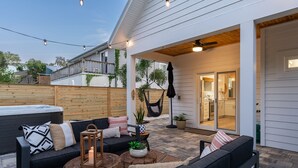 Une terrasse extérieure avec un canapé noir, des coussins, une petite table et un hamac.