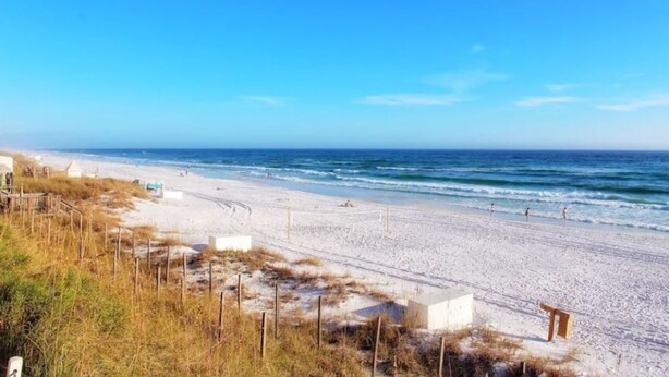 Een strand met een zandstrand, enkele personen en een helderblauwe lucht.