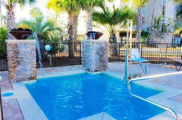 A swimming pool with stone pillars, a lounge chair, and a fence.