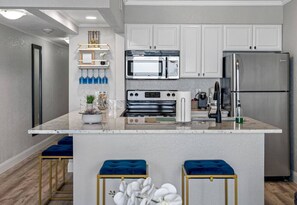 A modern kitchen with white cabinets, stainless steel appliances, a marble countertop, and blue bar stools.