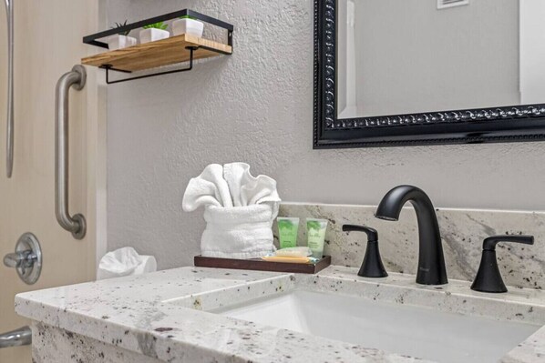 A bathroom with a sink, a mirror, a towel, and a shelf with toiletries.