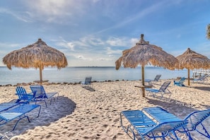A beach with thatched umbrellas and blue lounge chairs.