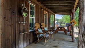 A wooden cabin with a porch, two rocking chairs, a table, and a mirror. - Cozy Chic Cabin on Texas Wine Trail (Stonewall)