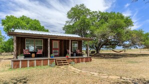 A rustic cabin with a porch, large windows, and a red door. - Cozy Chic Cabin on Texas Wine Trail (Stonewall)