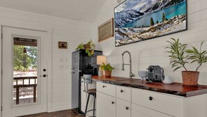 A kitchen with white cabinets, a wooden countertop, a sink, and a coffee machine. There is a door leading to an outdoor area with a view of trees and a mountain. - Cozy Chic Cabin on Texas Wine Trail (Stonewall)