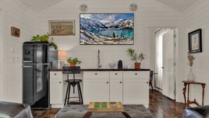 A modern kitchen with white cabinetry, a black refrigerator, and a large window overlooking a scenic mountain landscape. - Cozy Chic Cabin on Texas Wine Trail (Stonewall)