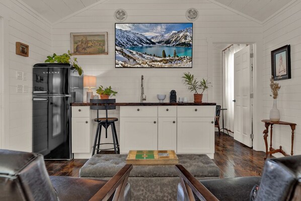 A modern kitchen with white cabinetry, a black refrigerator, and a large window overlooking a scenic mountain landscape.