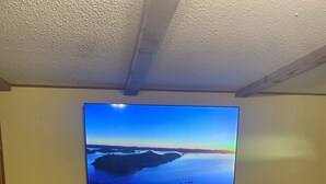 A room with a wooden floor, a TV mounted on the wall displaying a scenic landscape, a wooden console table with decorative items, and a tall floor lamp. - Minutes from Beautiful broken bow lake  (Broken Bow)