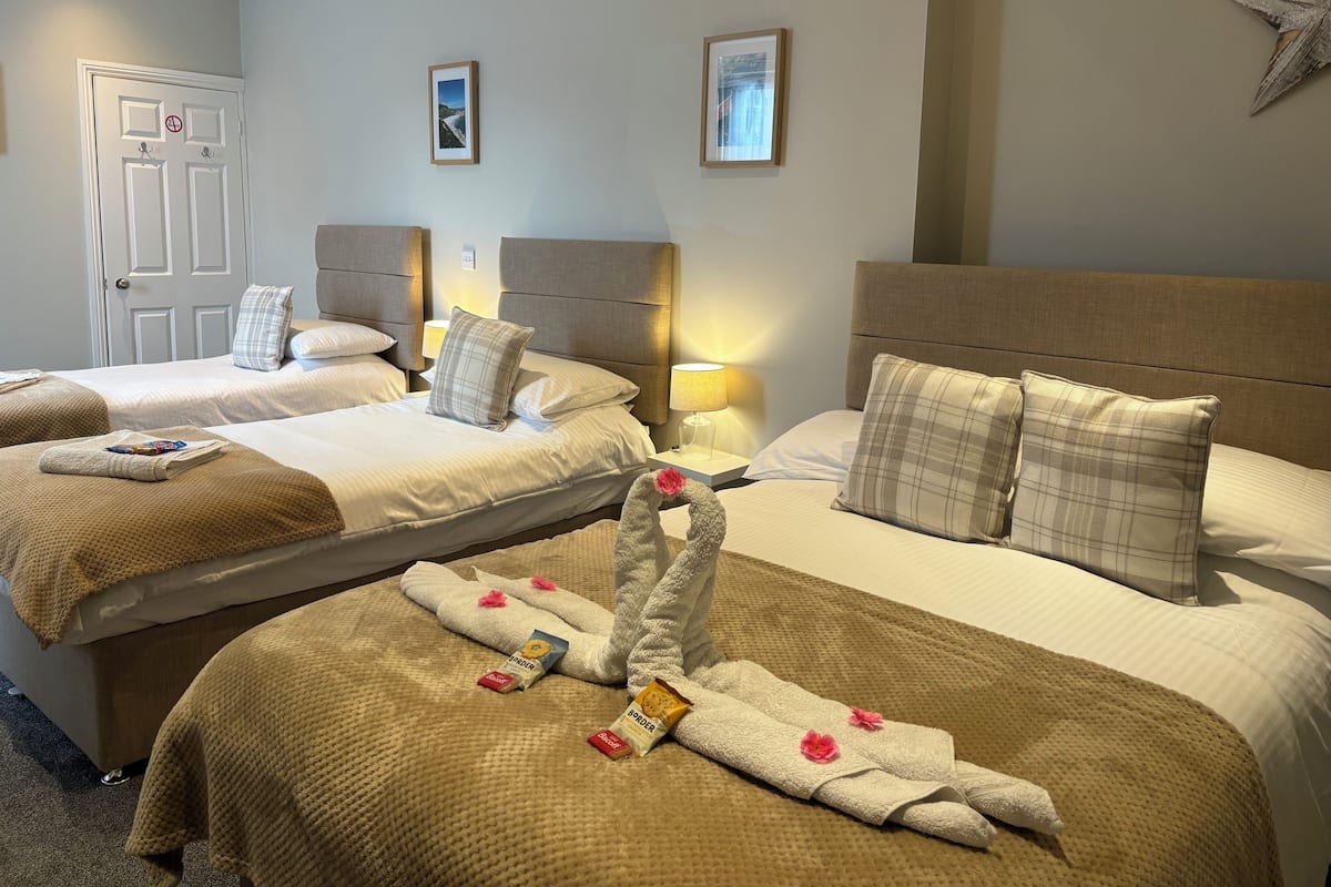 A hotel room with three beds, each with a headboard, bedside lamps, and a framed picture on the wall.