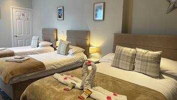 A hotel room with three beds, each with a headboard, bedside lamps, and a framed picture on the wall.