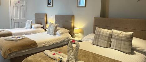A hotel room with three beds, each with a headboard, bedside lamps, and a framed picture on the wall.