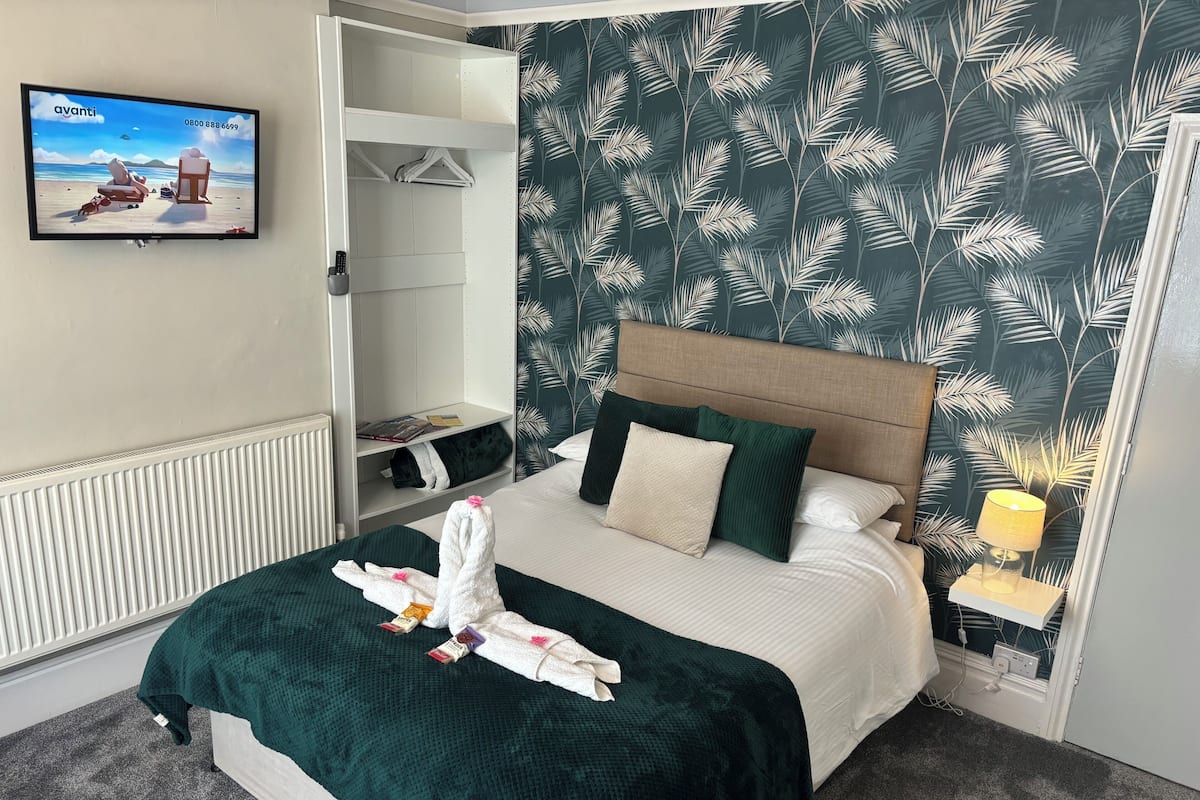 A hotel room with a bed, a TV, a wardrobe, and a patterned wall.
