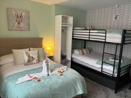 Una cama individual con cabecera, una mesita de noche con lámpara y una estantería en la pared.