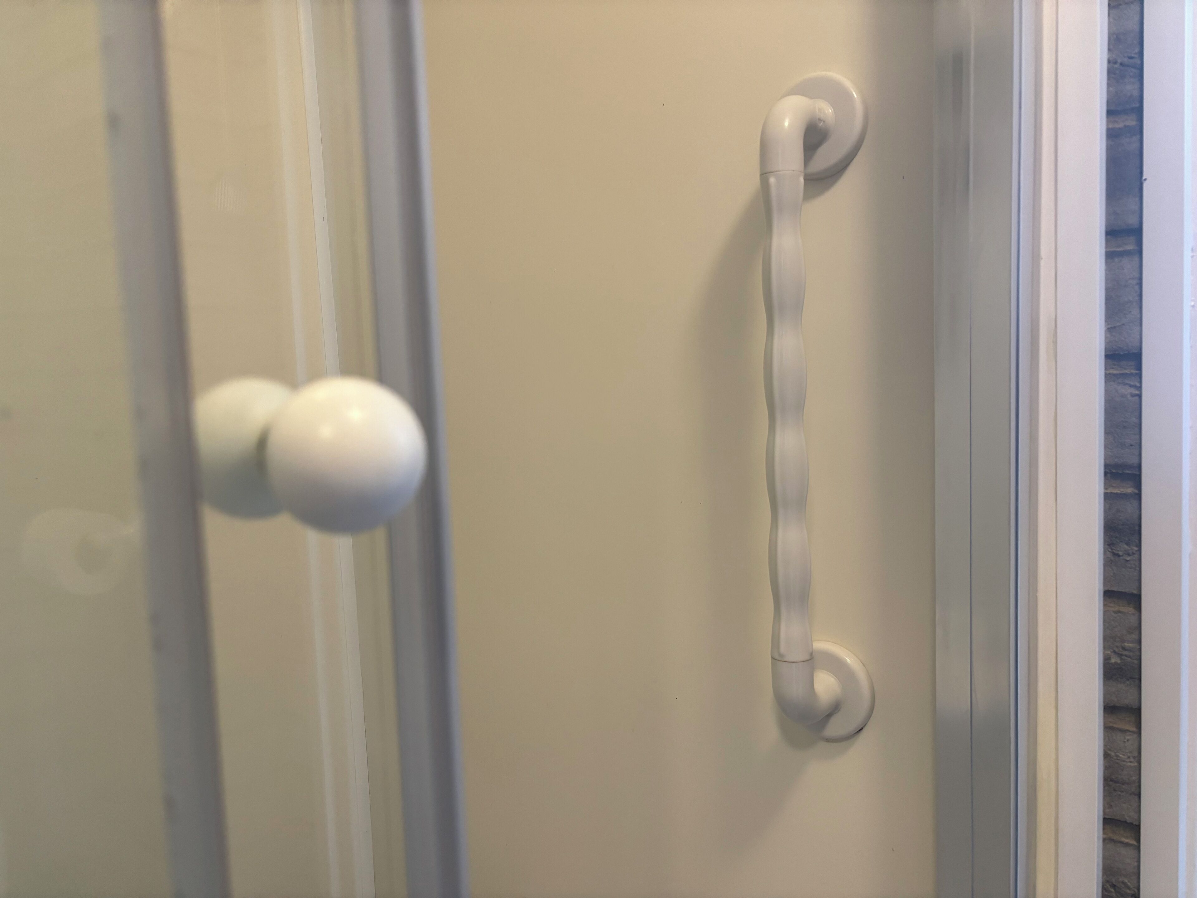 A bathroom with a white shower door, a white towel rack, and a white towel hanging on the wall.