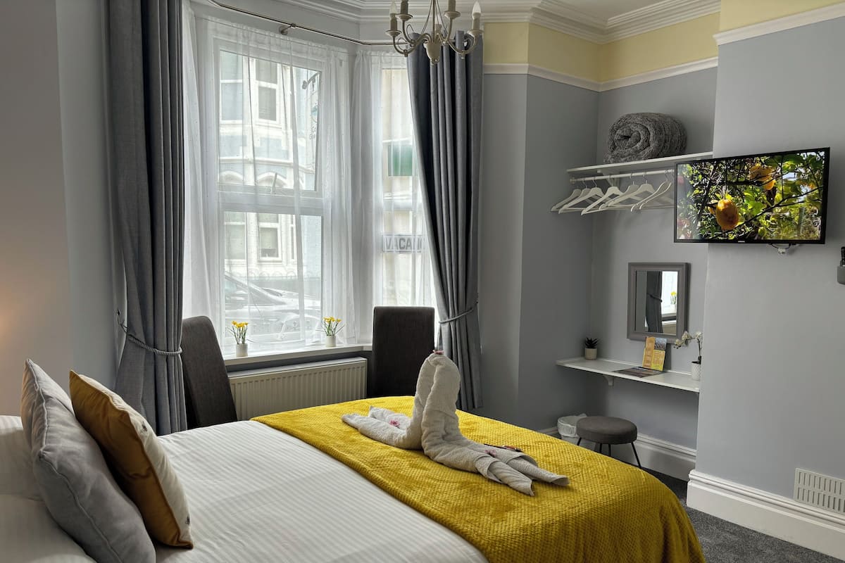 A hotel room with a bed, a TV, a small shelf, and a window with curtains.