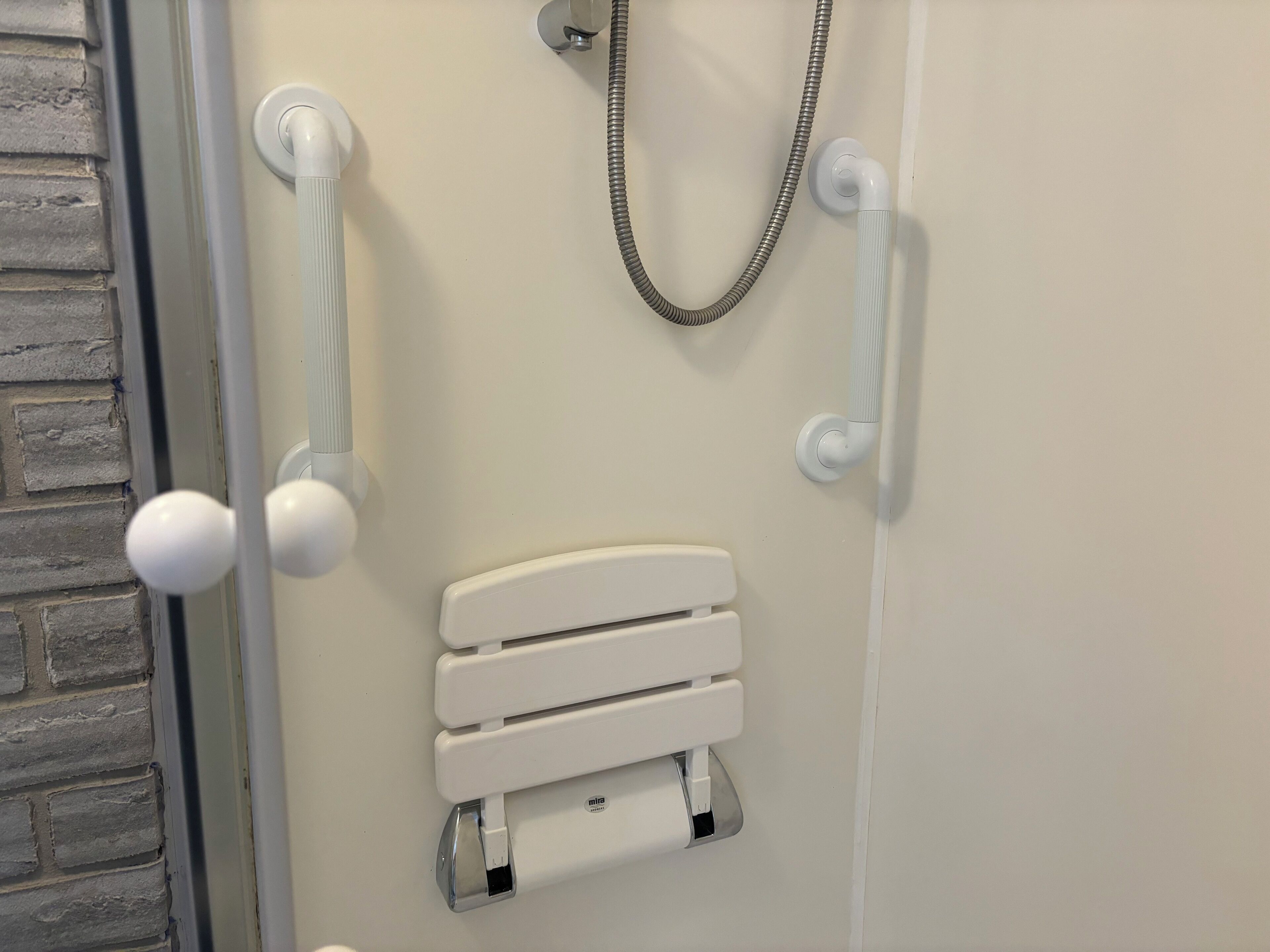 Une salle de bain avec un espace de douche blanc, une porte en verre et un radiateur blanc.