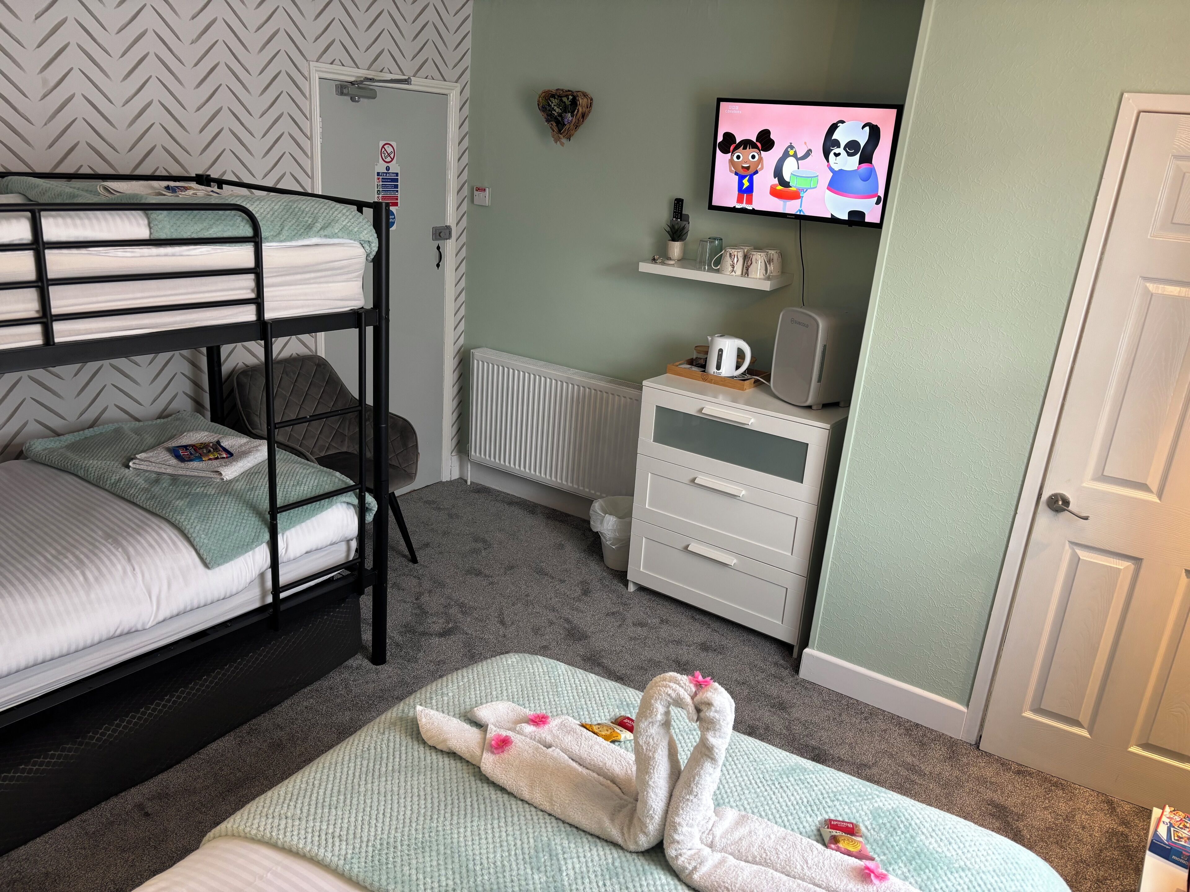 Une chambre avec un lit superposé, une télévision, une commode et un radiateur.