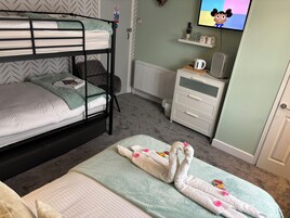 Una cama litera con un televisor encima, un aparador blanco y una manta suave en el suelo.