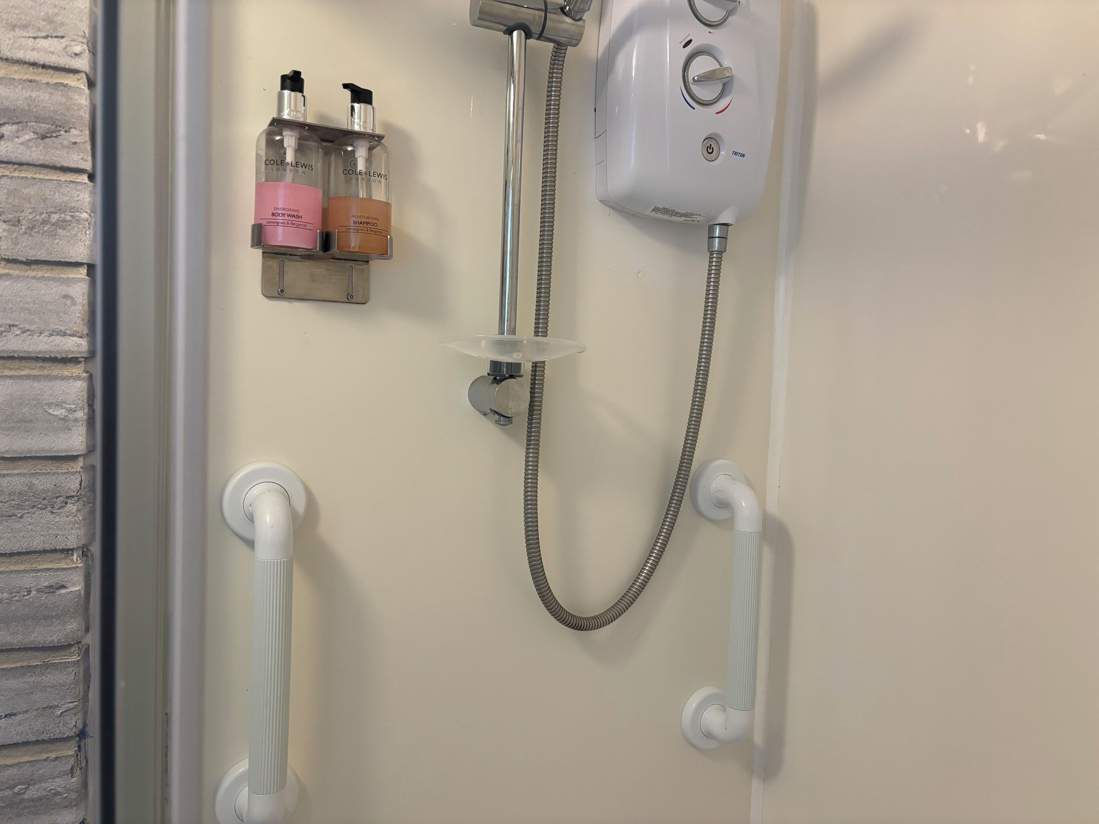 Un espace douche équipé d’un pommeau de douche à main, d’un flexible de douche et de deux bouteilles de shampoing.