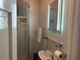 Un baño con cabina de ducha de vidrio, un lavamanos blanco con espejo y un perchero para toallas.