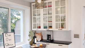 Een keuken met witte kastjes, een ronde tafel, twee krukken en een hanglamp.