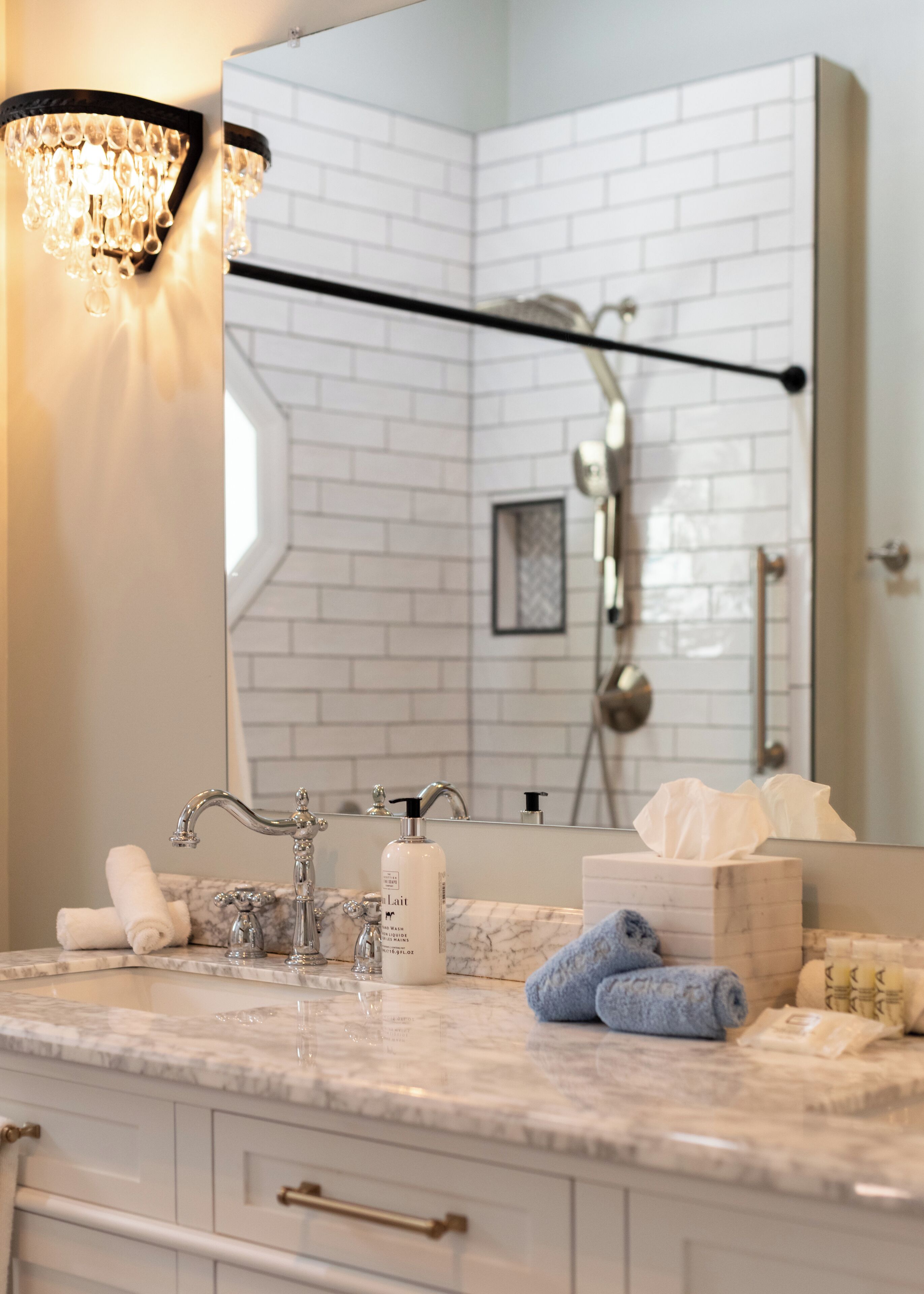 A bathroom with a marble countertop, a sink with a modern faucet, a mirror, and a shower area.