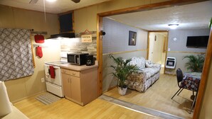 Un espacio habitable compacto con kitchenette, sofá, mesa de comedor y una planta en maceta.