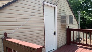 Una terraza de madera con una puerta blanca y una unidad de aire acondicionado instalada en la pared.
