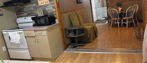 A compact kitchen with a microwave, stove, and a coffee maker on the counter. There is a dining area with a table and chairs, and a television mounted on the wall.