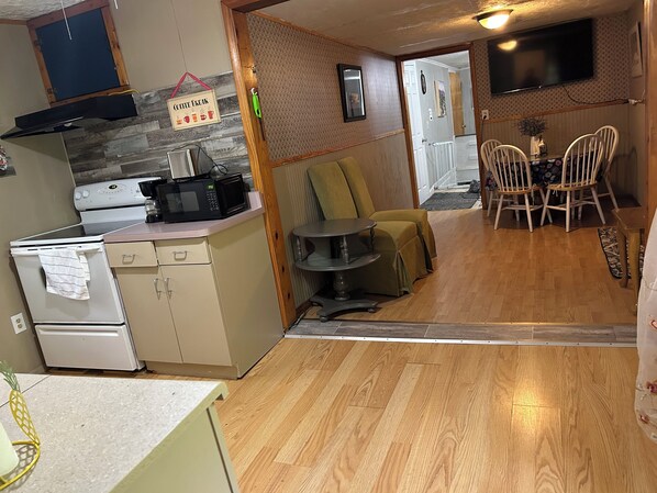 A compact kitchen with a microwave, stove, and a coffee maker on the counter. There is a dining area with a table and chairs, and a television mounted on the wall.