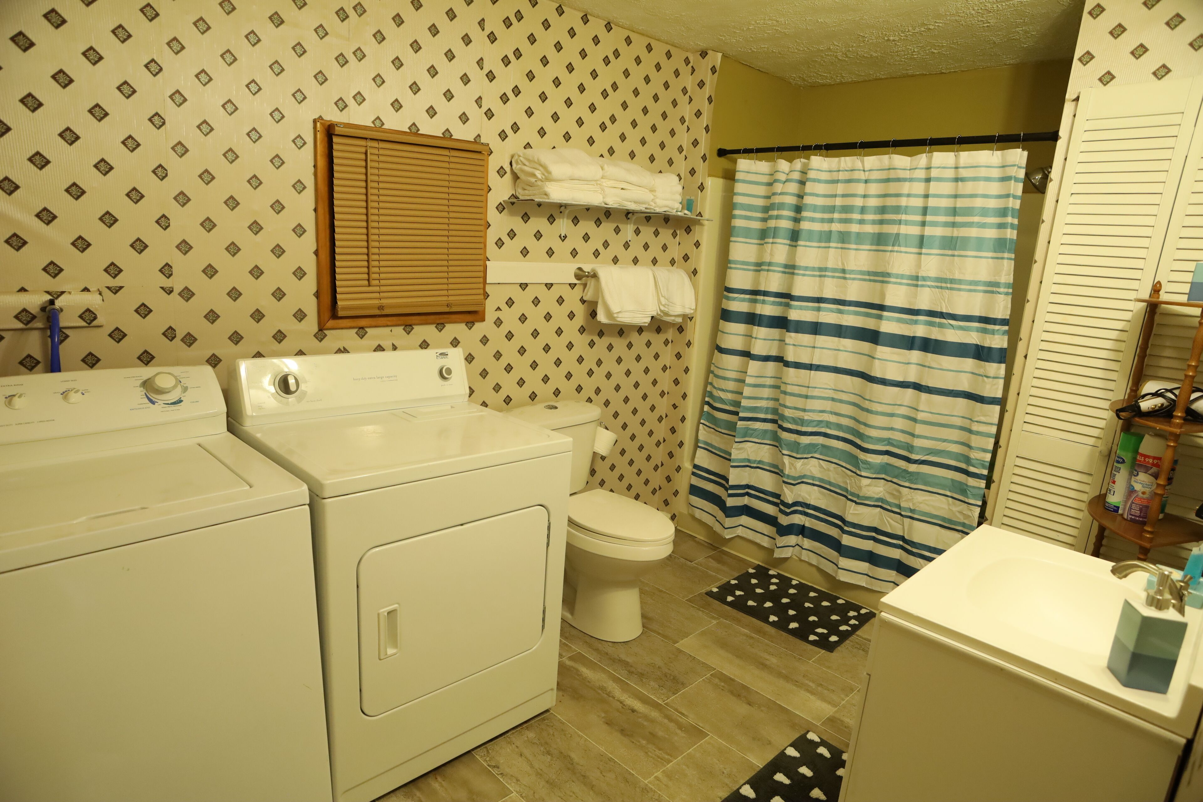 A bathroom with a washing machine, toilet, and a bathtub with a striped shower curtain.