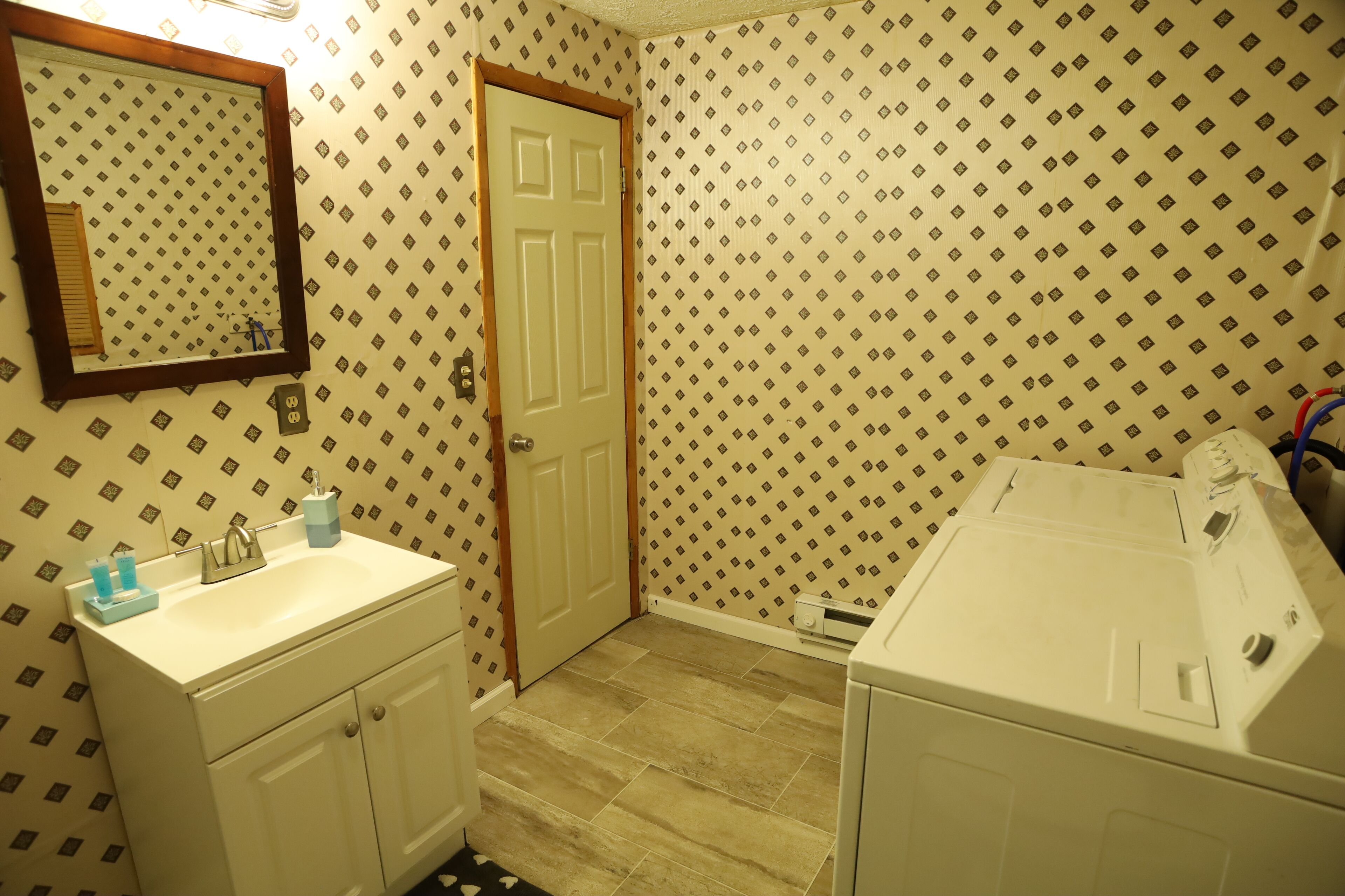 A bathroom with a sink, mirror, door, and a washing machine.
