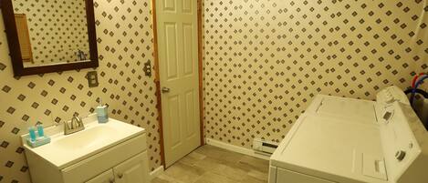 A bathroom with a sink, mirror, door, and a washing machine.