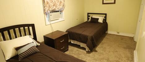 A bedroom with two single beds, a nightstand, a dresser, a window with a curtain, and a framed picture on the wall.