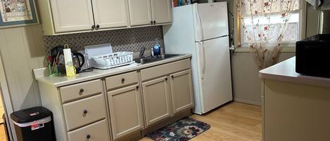 A kitchen with light-colored cabinets, a refrigerator, a sink, and a trash bin.