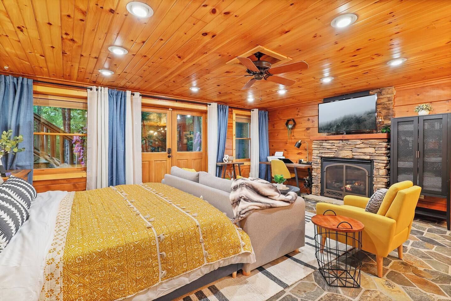 A cozy cabin interior with a bed, sofa, and a fireplace.