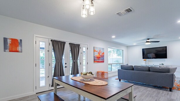 A modern living room with a wooden dining table, grey sofa, and a flat-screen TV.