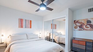 A bedroom with a bed, bedside tables, a ceiling fan, a dresser, and abstract wall art.