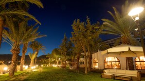 A well-lit outdoor area with a grassy lawn, palm trees, and a seating area with a canopy. - Elysium Garden (Bozyazi)