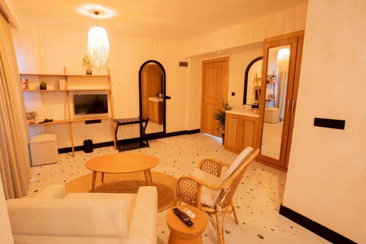 Ein Hotelzimmer mit einer Sitzecke, einem runden Tisch, einem Fernseher, einer kleinen Küchenzeile und einem Spiegel.