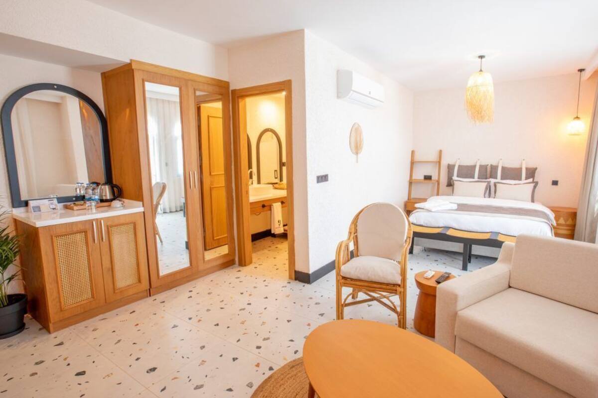 Ein Hotelzimmer mit Bett, Sofa, Sessel, Schreibtisch mit Spiegel und einer Zimmerpflanze.