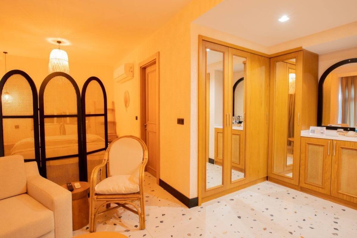 Ein Hotelzimmer mit Sofa, Sessel und einem kleinen Tisch. Es gibt einen Spiegel, einen Kleiderschrank und eine Tür zu einem weiteren Raum.