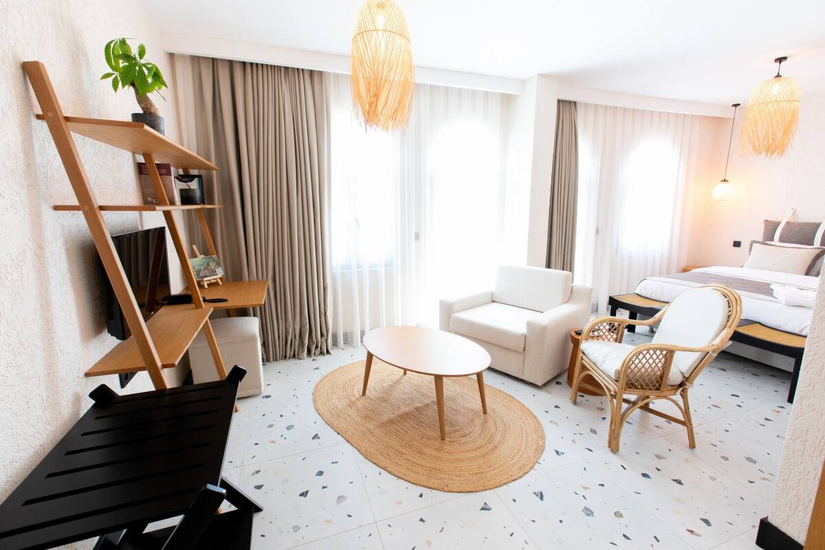 Ein modernes Hotelzimmer mit einer Sitzecke, einem runden Tisch, einem Korbstuhl, einem Bett und einer Pflanze.