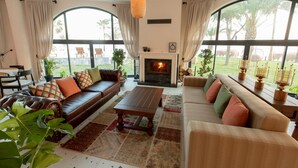 A spacious living room with a fireplace, leather sofas, and large windows offering a view of the outdoors. - Elysium Garden (Bozyazi)