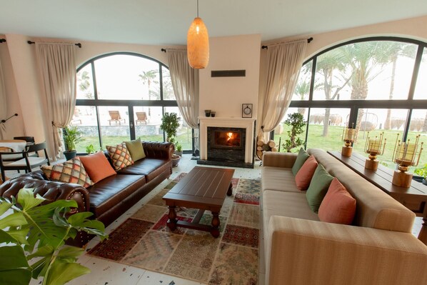 A spacious living room with a fireplace, leather sofas, and large windows offering a view of the outdoors. - Elysium Garden (Bozyazi)