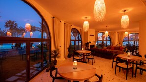 A well-lit indoor space with round tables and chairs, large windows, and hanging light fixtures. - Elysium Garden (Bozyazi)