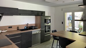 Une cuisine moderne équipée d’un lave-vaisselle, d’un four et d’un évier. Un coin repas avec une table et des chaises est également disponible.
