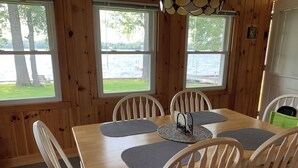 Ein Esszimmer mit Holzboden, einem Tisch und Stühlen, großen Fenstern mit Seeblick und einer hängenden Leuchte.