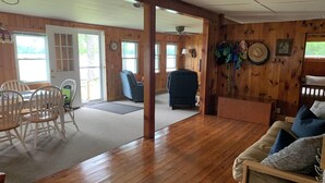 Ein geräumiges Zimmer mit Holzböden, einem Essbereich mit weißen Stühlen, einem blauen Sofa und einem Deckenventilator.